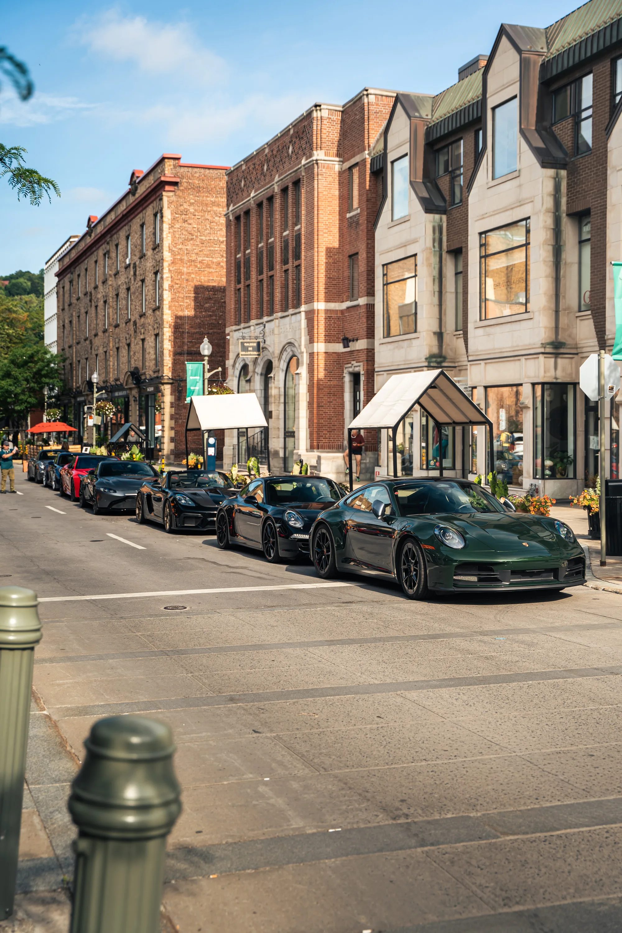 Greene Avenue from the sidewalk: a line of parked sports cars at the curb in front of Westmount’s brick and limestone shopfronts.