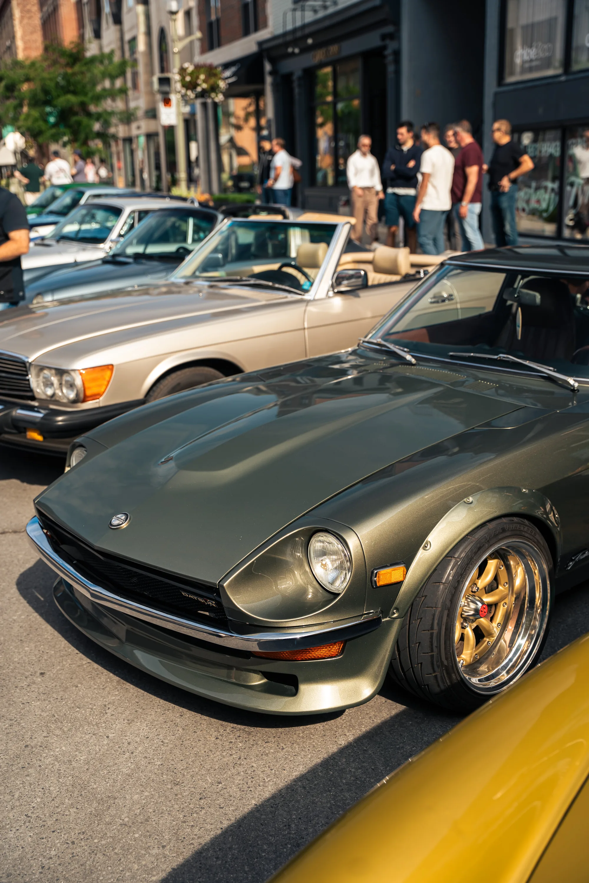 A green Datsun Z on gold wheels, a beige Mercedes-Benz SL parked behind it.